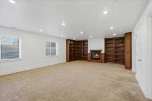 Unfurnished living room featuring recessed lighting, a glass covered fireplace, light carpet, and built in features