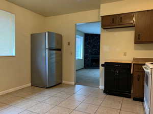 Kitchen with freestanding refrigerator, white stove, light countertops, a stone fireplace, and light tile patterned floors