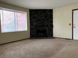 Unfurnished living room with carpet floors, a stone fireplace, and a textured ceiling