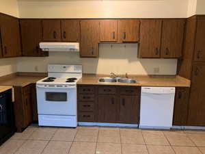 Kitchen with white appliances, under cabinet range hood, dark brown cabinets, light countertops, and light tile patterned floors