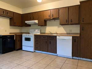 Kitchen with white appliances, dark brown cabinetry, under cabinet range hood, and light tile patterned floors
