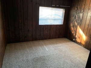 Unfurnished room featuring wooden walls and carpet