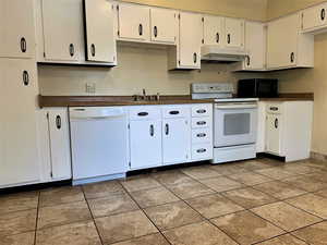Kitchen with dark countertops, white appliances, white cabinets, and under cabinet range hood
