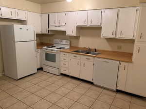 Kitchen with white appliances, light countertops, white cabinets, and under cabinet range hood