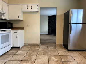 Kitchen with freestanding refrigerator, electric stove, white cabinets, a textured ceiling, and a fireplace