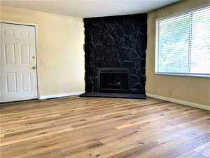 Unfurnished living room with a stone fireplace, light wood finished floors, and a textured ceiling