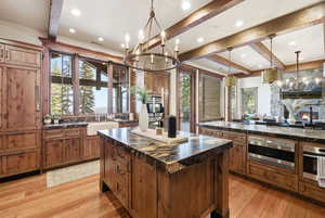 Kitchen featuring a center island, a chandelier, beamed ceiling, brown cabinetry, and pendant lighting