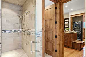 Full bathroom with a shower stall, stacked washer and clothes dryer, light wood-style flooring, and recessed lighting