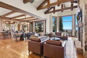 Living room featuring high vaulted ceiling, light wood-style flooring, beamed ceiling, a stone fireplace, and a chandelier
