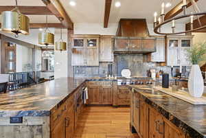 Kitchen featuring glass insert cabinets, pendant lighting, brown cabinets, decorative backsplash, and a peninsula