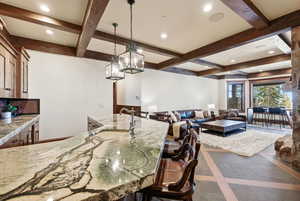 Kitchen with inlaid floor details, recessed lighting, beamed ceiling, decorative light fixtures, and light stone countertops