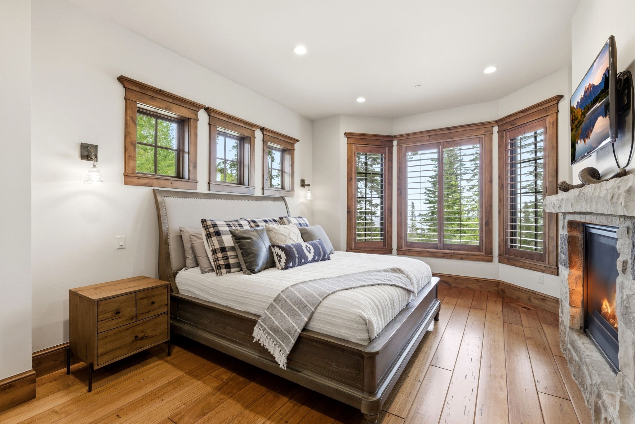 Spacious room featuring wood-finish flooring, a stone fireplace with hearth, recessed lighting, and multiple windows with wood trim and plantation shutters