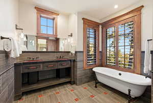 Full bathroom with a wainscoted wall, double vanity, a freestanding tub, and tile walls