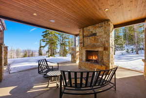 Snow covered patio featuring an outdoor stone fireplace and a patio