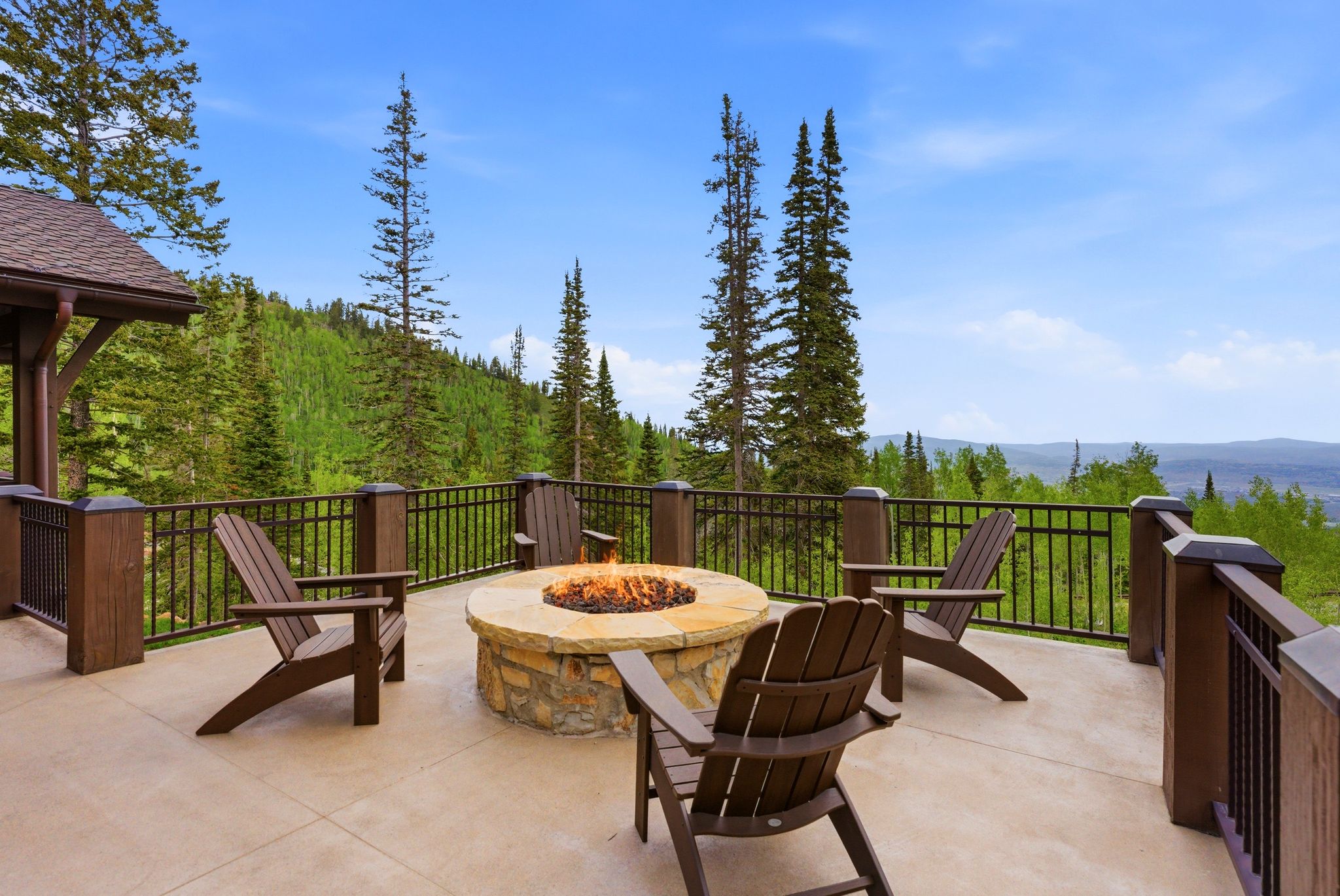 Expansive outdoor patio featuring a stone-clad fire pit, concrete surface, and wrought iron railing