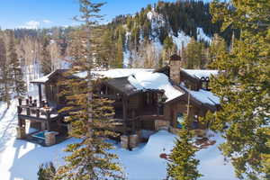 View of snowy exterior featuring a chimney, a deck, and a view of trees