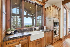 Kitchen workstation featuring a farmhouse sink, stone countertops, and wood-finish cabinetry