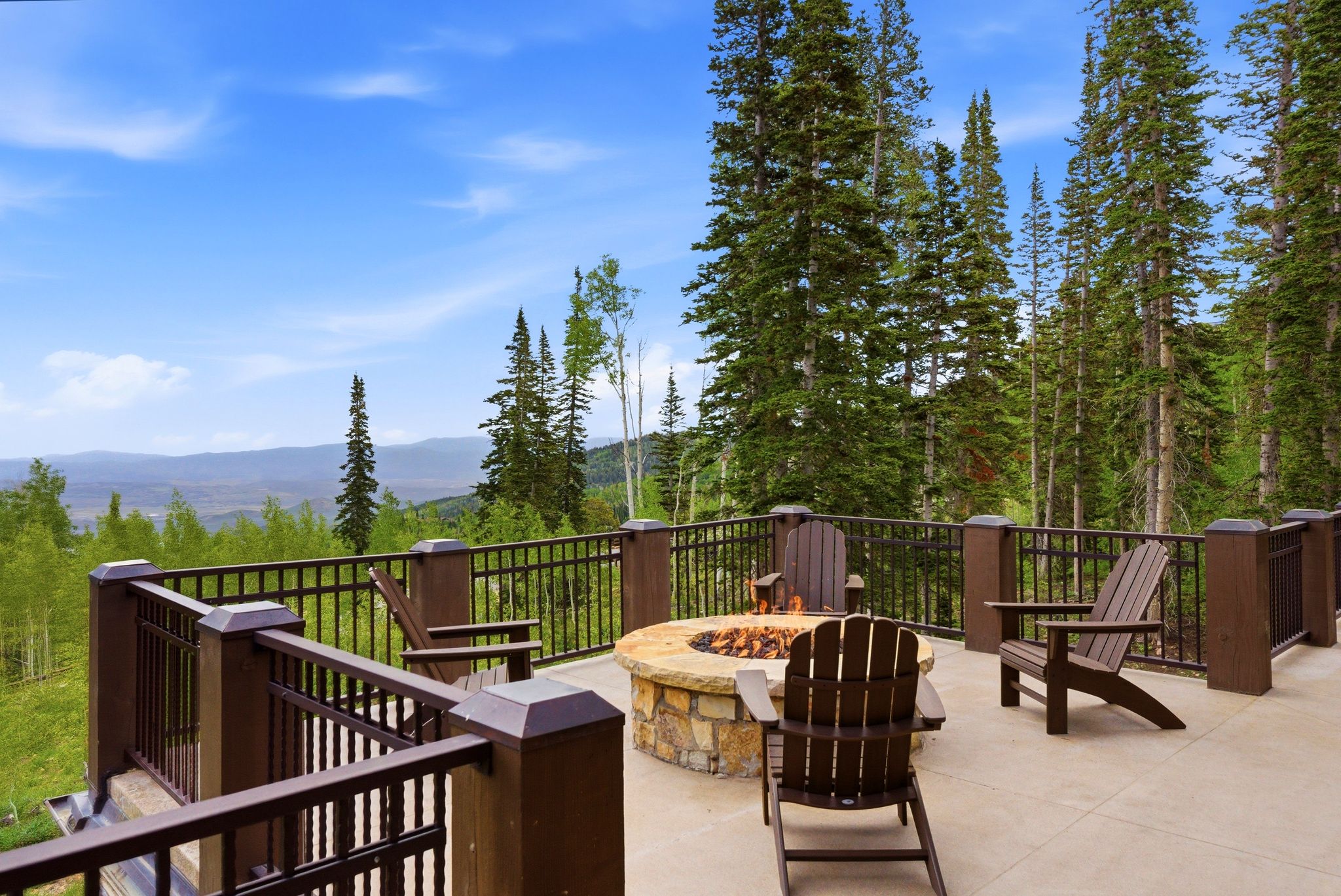 Expansive outdoor patio featuring a built-in stone fire pit, concrete flooring, and metal railings