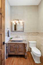 Half bath featuring vanity, tile walls, a wainscoted wall, and wood finished floors