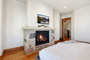 Bedroom with hardwood / wood-style floors, a stone fireplace, and recessed lighting