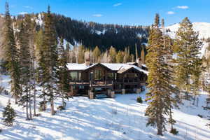 Snow covered rear of property featuring a chimney, a wooden deck, and a view of trees