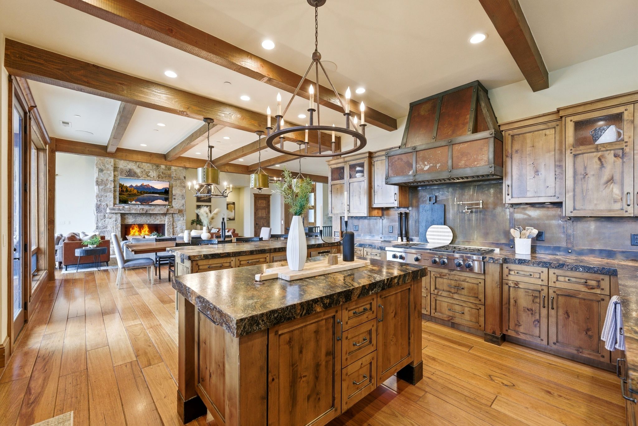 Gourmet kitchen featuring a substantial wood-finish island with stone countertop, stainless steel range with copper-clad hood, distressed wood cabinetry, and wood-finish flooring