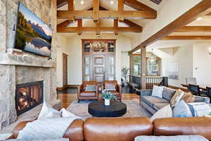 Living room featuring high vaulted ceiling, a stone fireplace, wood finished floors, a chandelier, and beamed ceiling