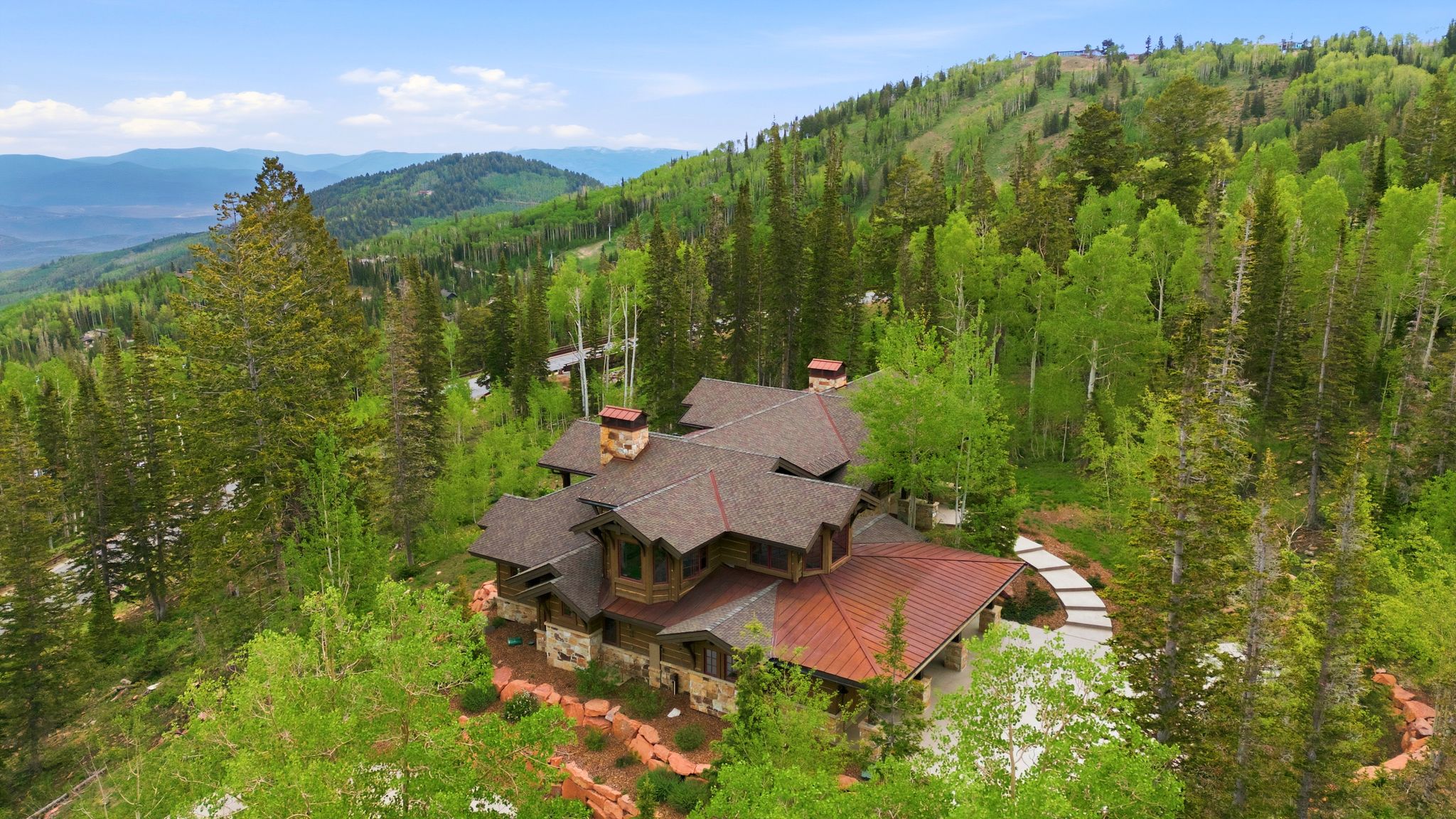 Multi-level residence featuring stone and wood siding, a multi-gabled roofline with exposed eaves, and a copper-toned metal roof section