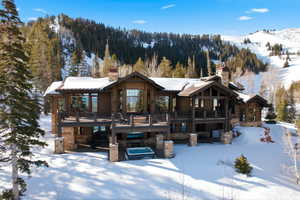 Snow covered rear of property featuring a chimney, log veneer siding, a wooden deck, and stone siding