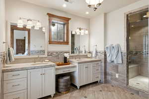 Full bath with two vanities, a shower stall, tile walls, wainscoting, and ensuite bathroom