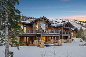 Snow covered house featuring a chimney, a patio area, and stone siding