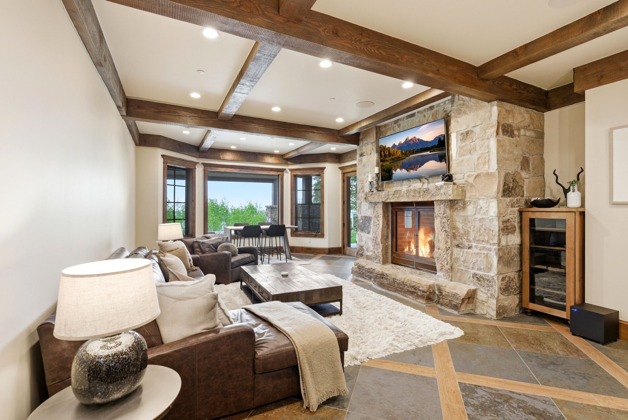 Stone fireplace with an integrated television niche, wood-finish ceiling beams, recessed lighting, expansive windows, and geometric pattern tile flooring