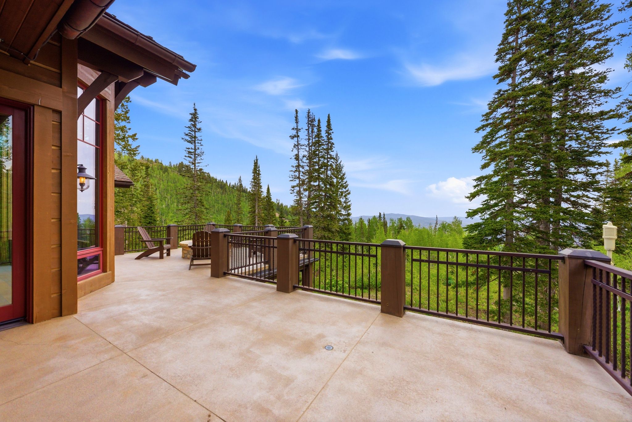 Expansive outdoor deck with concrete flooring, framed by a dark metal railing and wood posts