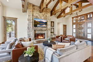 Living area featuring high vaulted ceiling, a stone fireplace, hardwood / wood-style floors, beam ceiling, and a chandelier