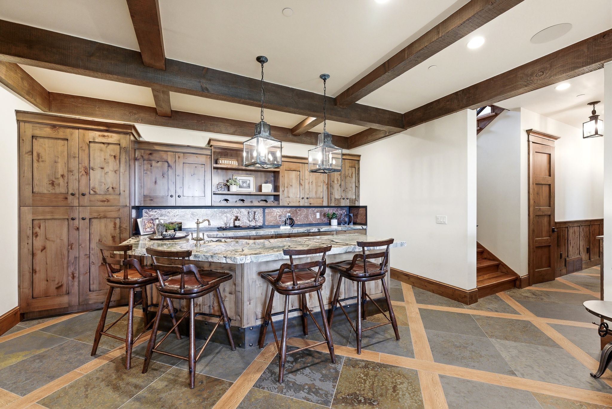 Custom kitchen island with stone countertop, accompanied by wooden cabinetry and exposed ceiling beams