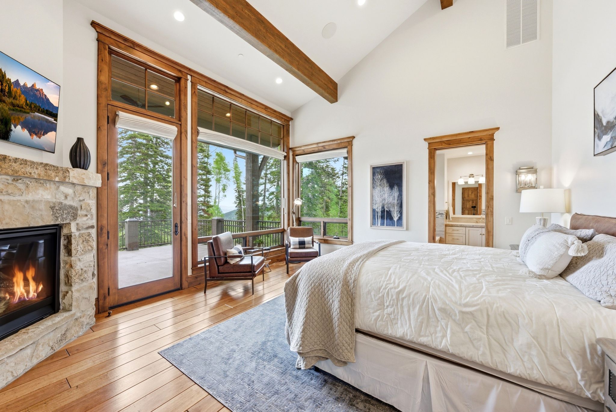 Vaulted ceiling room featuring a stone fireplace, wood-finish flooring, exposed wood beams, and a large glass door opening to an outdoor area