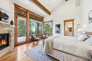 Vaulted ceiling room featuring a stone fireplace, wood-finish flooring, exposed wood beams, and a large glass door opening to an outdoor area
