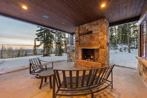 Snow covered patio with a patio area and an outdoor stone fireplace