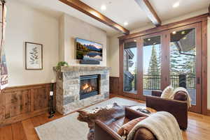 Living room with beamed ceiling, light wood-style flooring, a wainscoted wall, and a fireplace