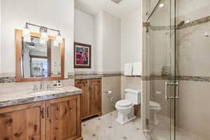 Full bathroom with vanity, a stall shower, a ceiling fan, a wainscoted wall, and light tile patterned flooring