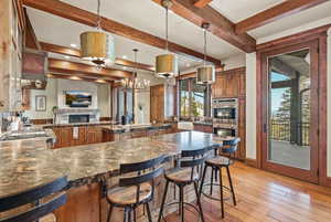 Kitchen with pendant lighting, brown cabinetry, light wood-type flooring, double oven, and a fireplace