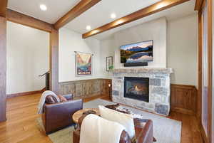Living room featuring hardwood / wood-style flooring, a stone fireplace, wainscoting, recessed lighting, and beam ceiling