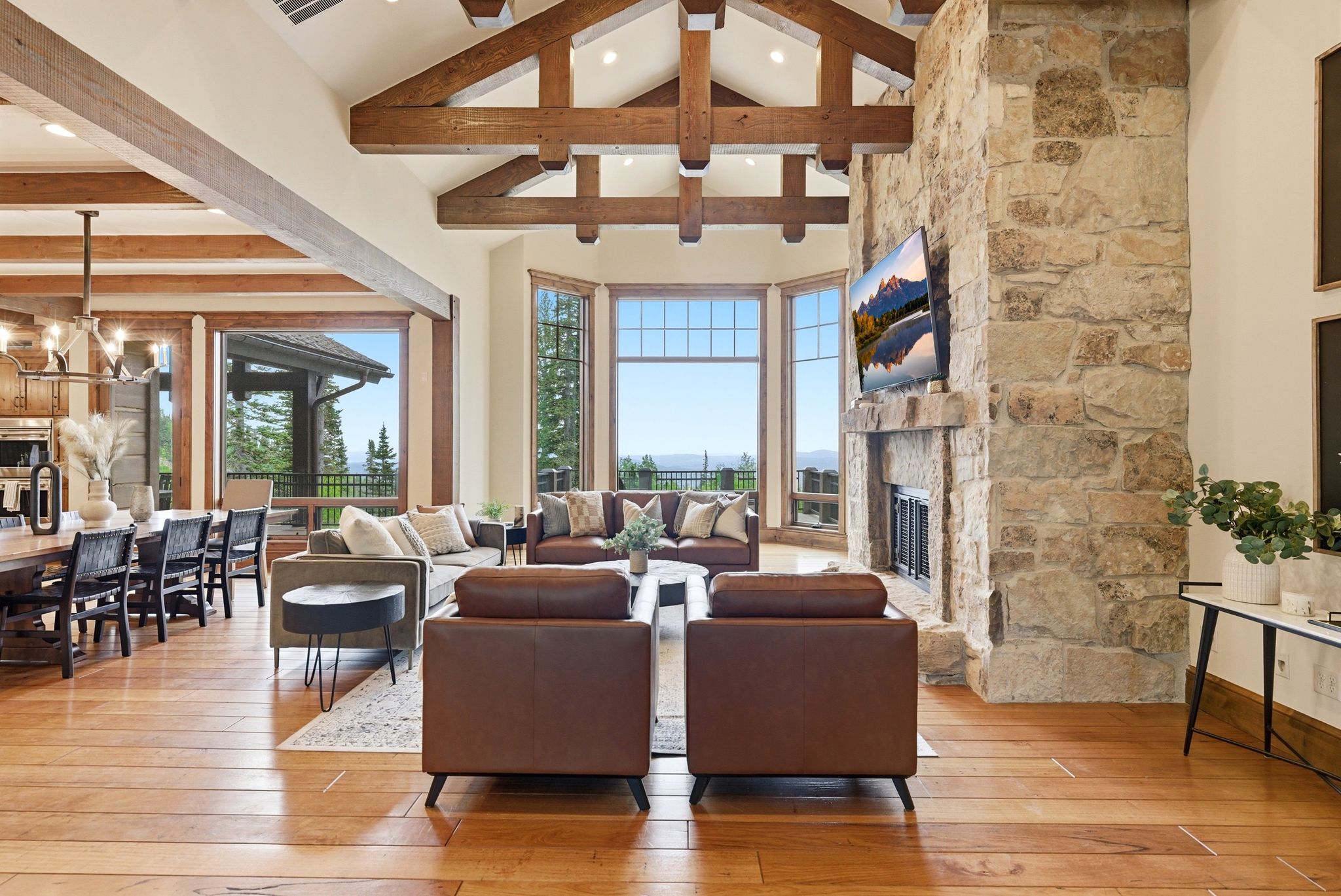Spacious living area featuring exposed wood beams, a stone-clad fireplace with integrated hearth, expansive windows, and wood-finish flooring