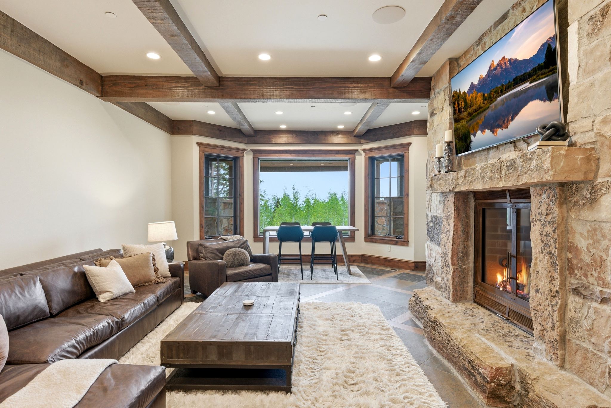 Stone-clad fireplace with a hearth, wood-beamed ceiling, recessed lighting, and bay windows