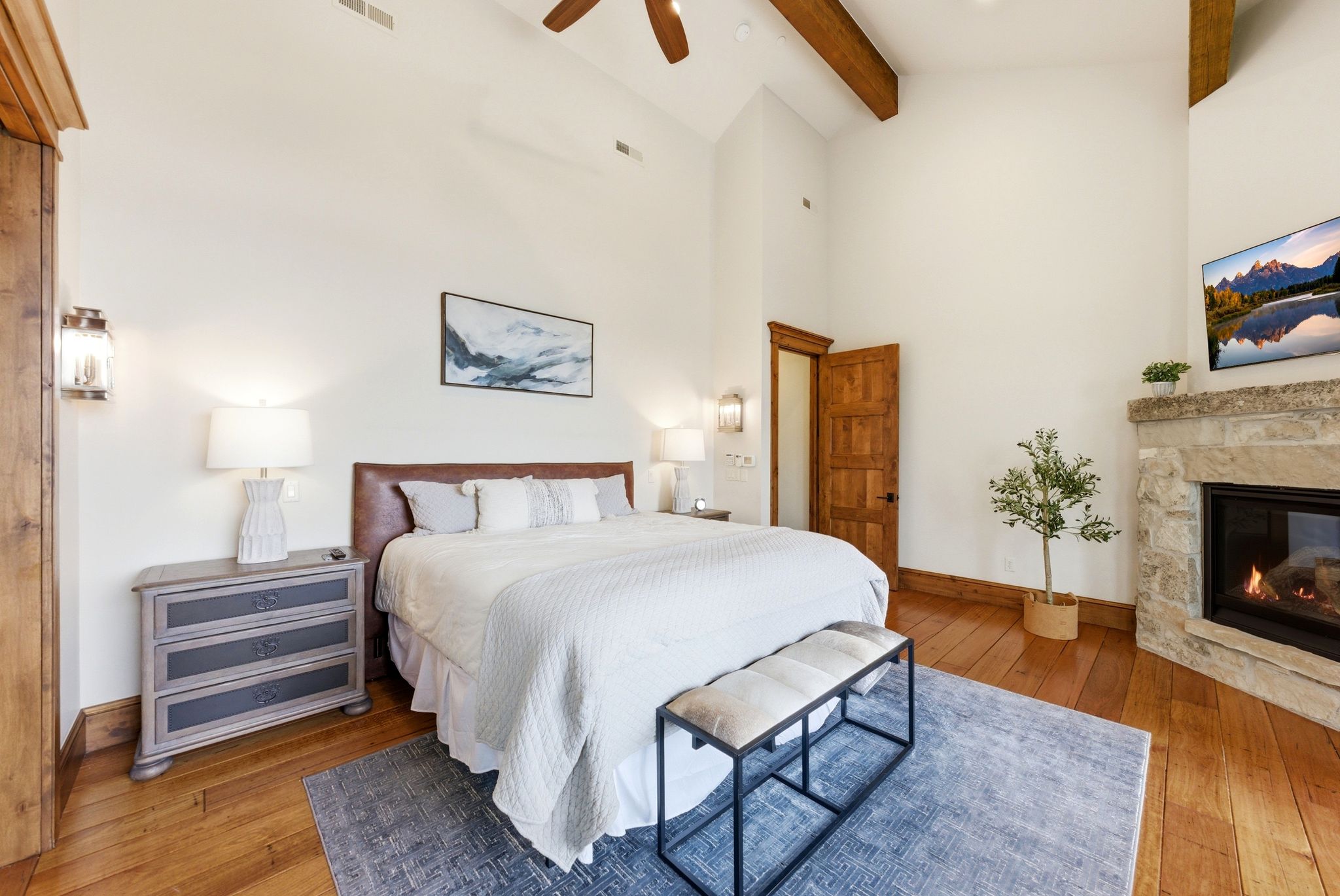 Spacious bedroom with vaulted ceilings, exposed wood beams, a stone-clad fireplace, and hardwood flooring