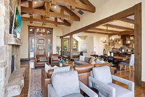 Living area with a chandelier, beam ceiling, wood-type flooring, high vaulted ceiling, and a fireplace