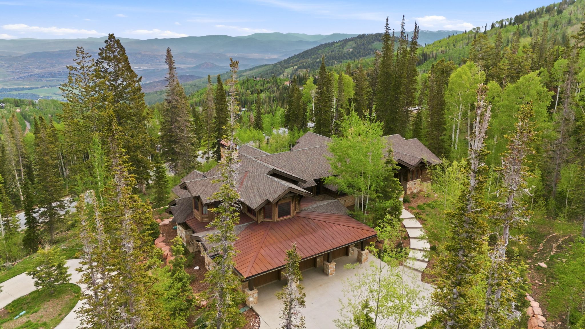 Mountain property featuring a multi-level design with a prominent copper-toned metal roof section, a stone and wood exterior, and a shingle roof