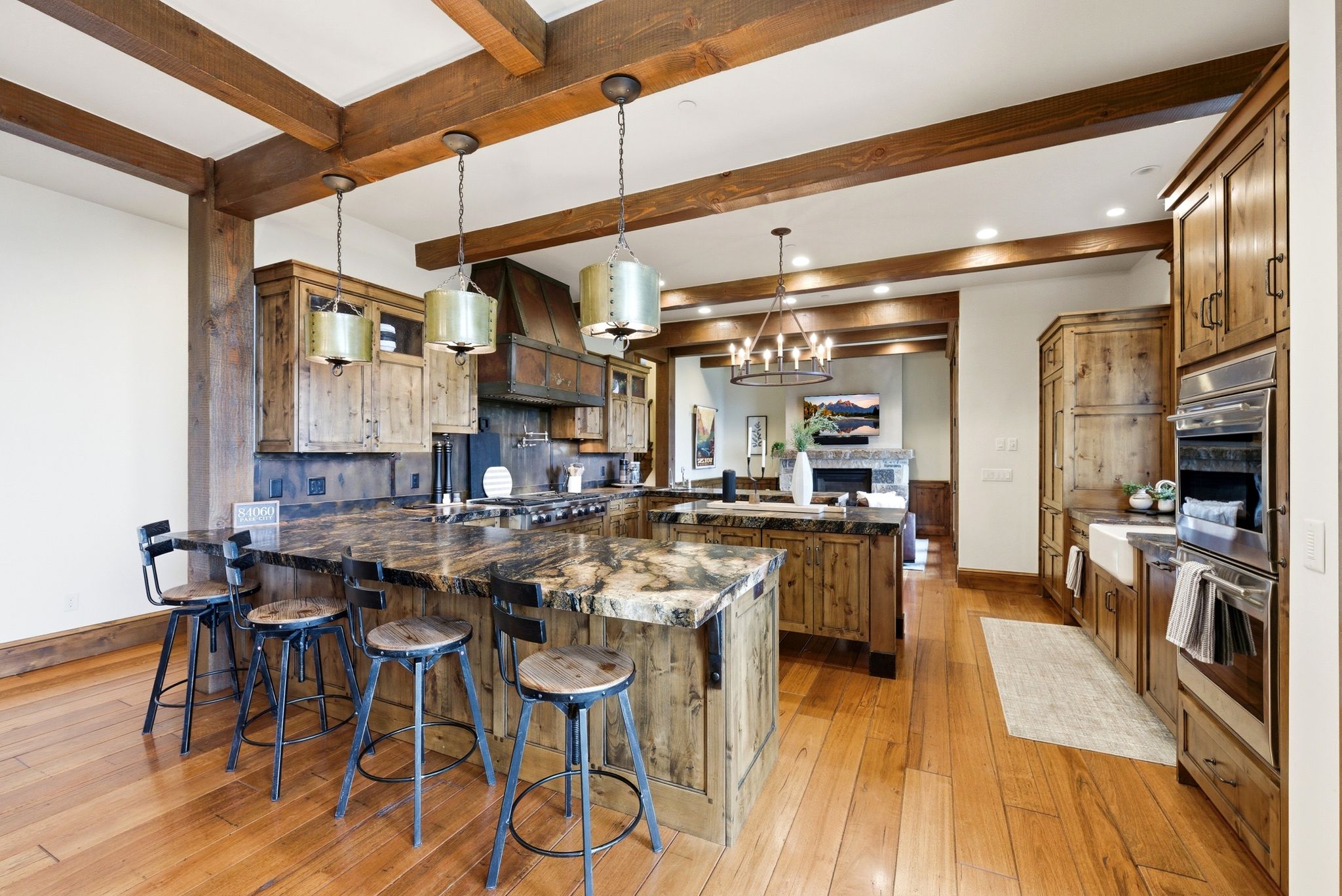 Spacious kitchen featuring exposed wood beams, wood-finish flooring, custom wood cabinetry, a large kitchen island with counter seating, and integrated stainless steel appliances