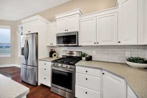 Kitchen featuring appliances with stainless steel finishes, white cabinetry, dark wood-type flooring, and decorative backsplash