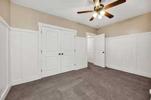 Unfurnished bedroom featuring a decorative wall, carpet floors, wainscoting, a closet, and a ceiling fan